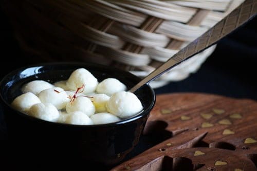 Ricotta cheese rasgulla is served chilled in a black bowl.