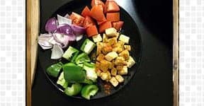 Diced onion, tomato, green bell pepper, and paneer cubes are kept in the black plate.