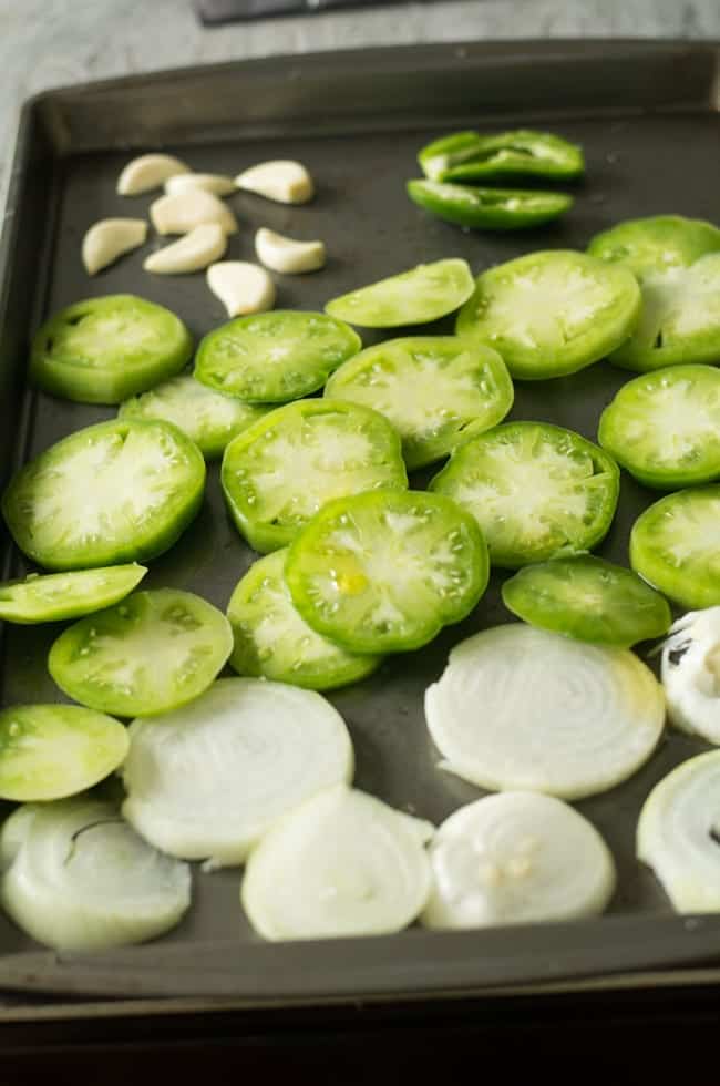 Arrange the vegetable slices on the tray. Slice the onion for about the same half an inch of thickness to make green tomato salsa.