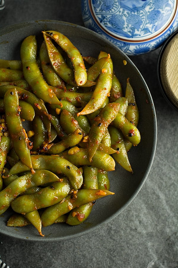 spicy chili garlic sauce coated edamame in black bowl.