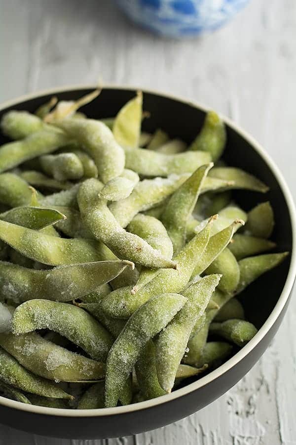 frozen edamame ready to steam in balck bowl for making spicy garlic edamame..