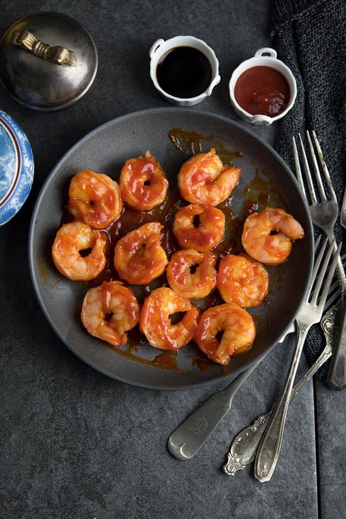 Spicy Sriracha shrimp is ready to eat served in a black plate with forks. A crowd pleasing recipe.