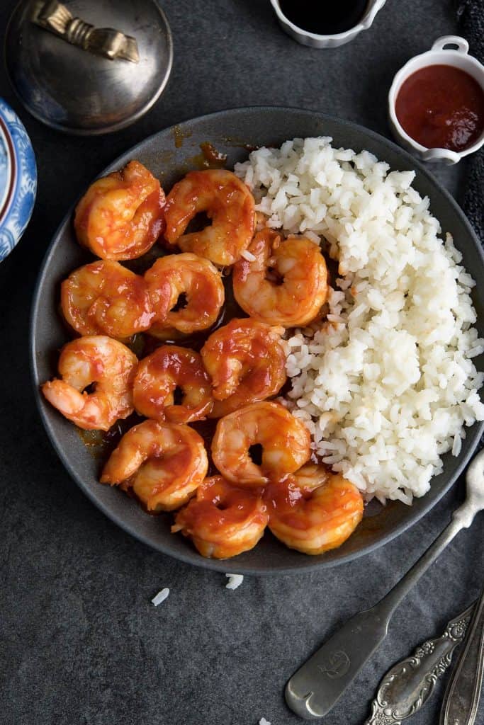 Honey Sriracha shrimp is placed over a black plate and served with rice.