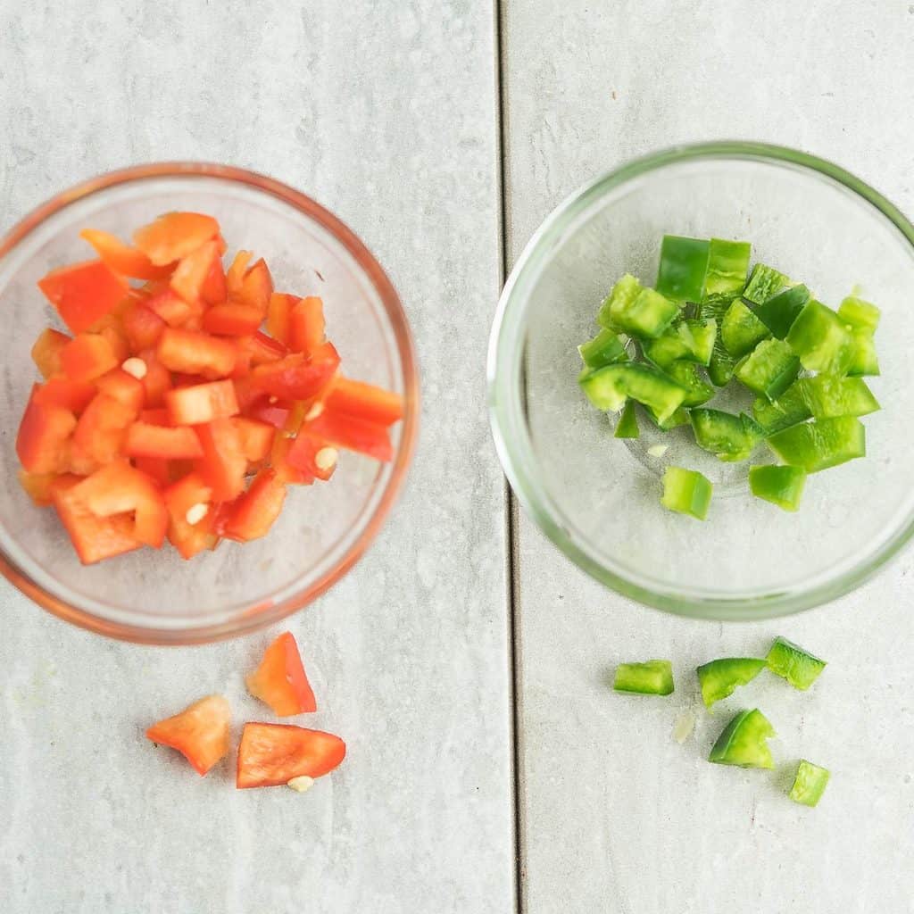 red pepper and jalapeno are chopped, in a clear bowl for prepping fiesta corn salad