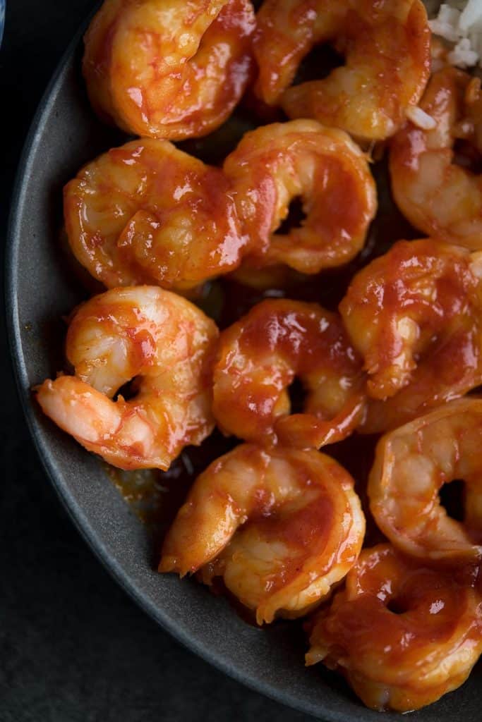 Juicy and glossy delectable hot and spicy Sriracha shrimp in a close up view.