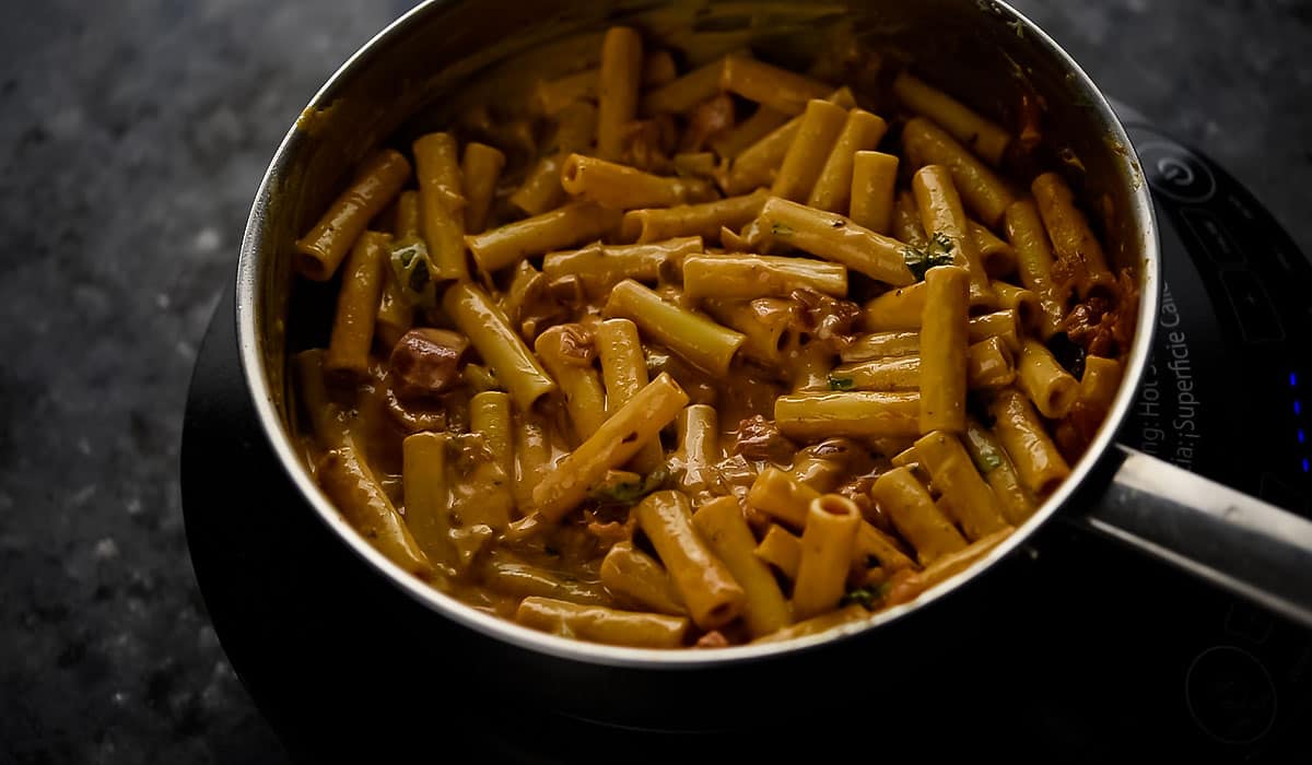 tossing the pasta in the sauce placed in the pan