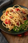 jalapeno spaghetti served in a plate with tomatoes and jalapeno slices