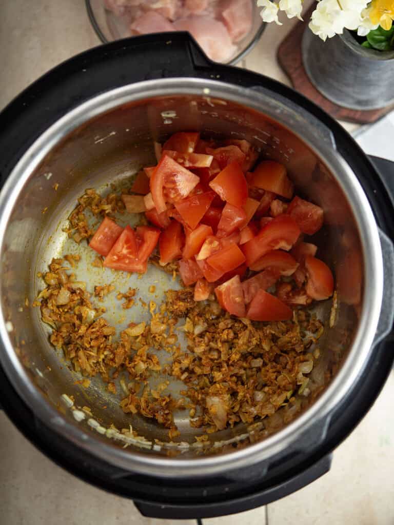 adding chopped tomato to onion for making Instant pot chicken curry