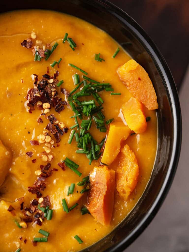 spicy butternut squash soup garnished with red pepper flakes served in a black bowl