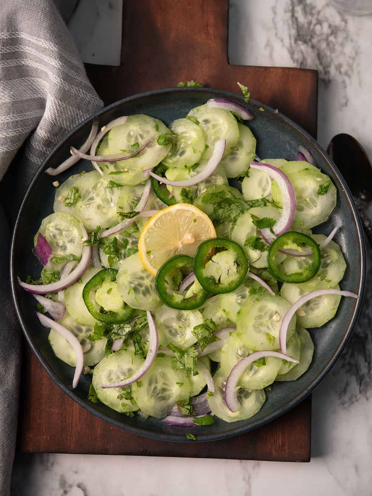 cucumber jalapeno salad served in a plate garnished with lemon slices, onion, and jalapeno slices.
