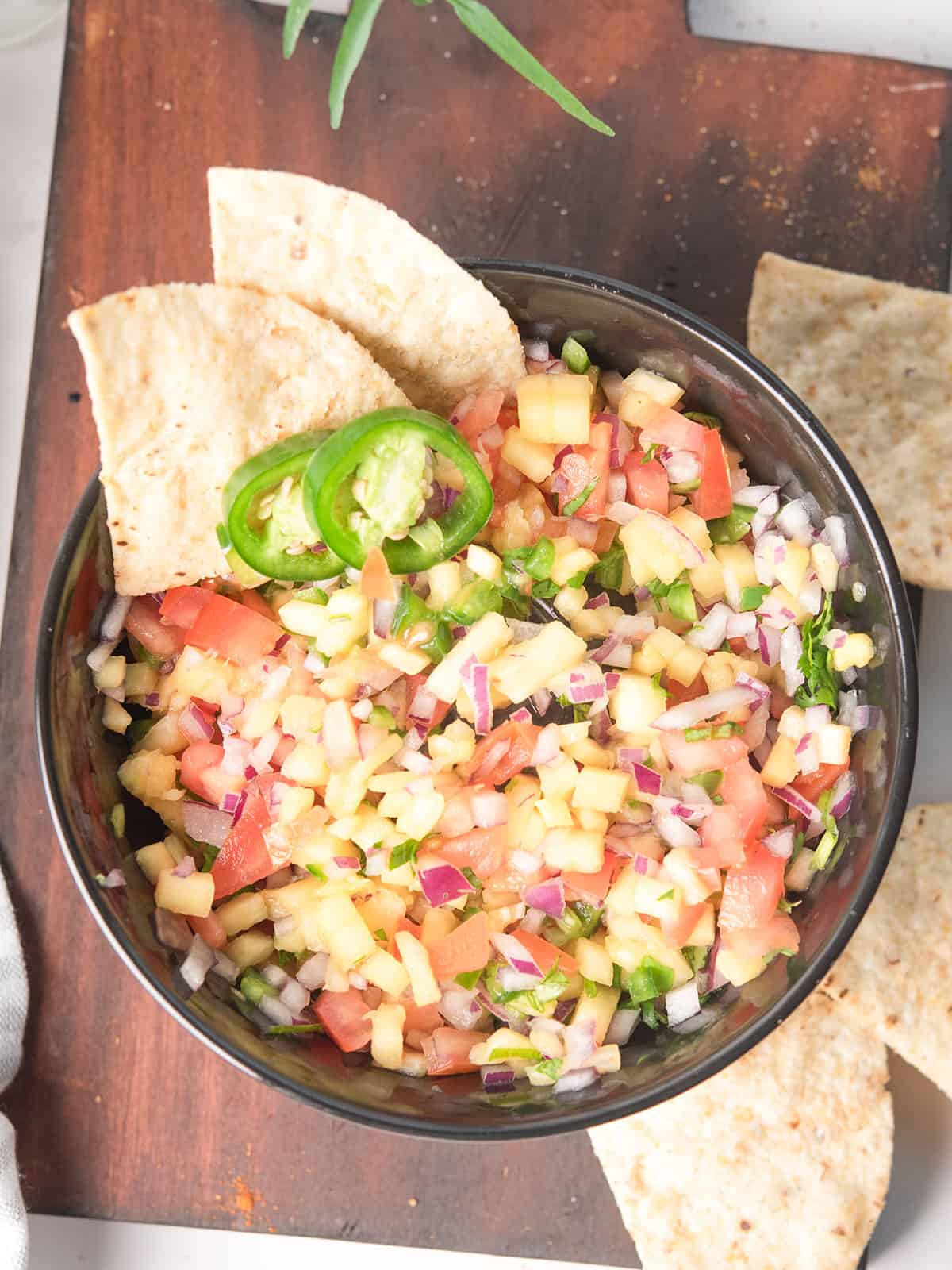 Pineapple Pico De Gallo served in a bowl with chips, and garnished with jalapeno slices