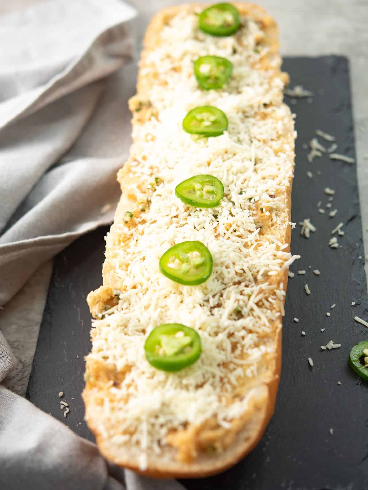 cheese sprinkled over the bread load with jalapeno pepper slices as garnish, ready to bake for making jalapeno garlic bread