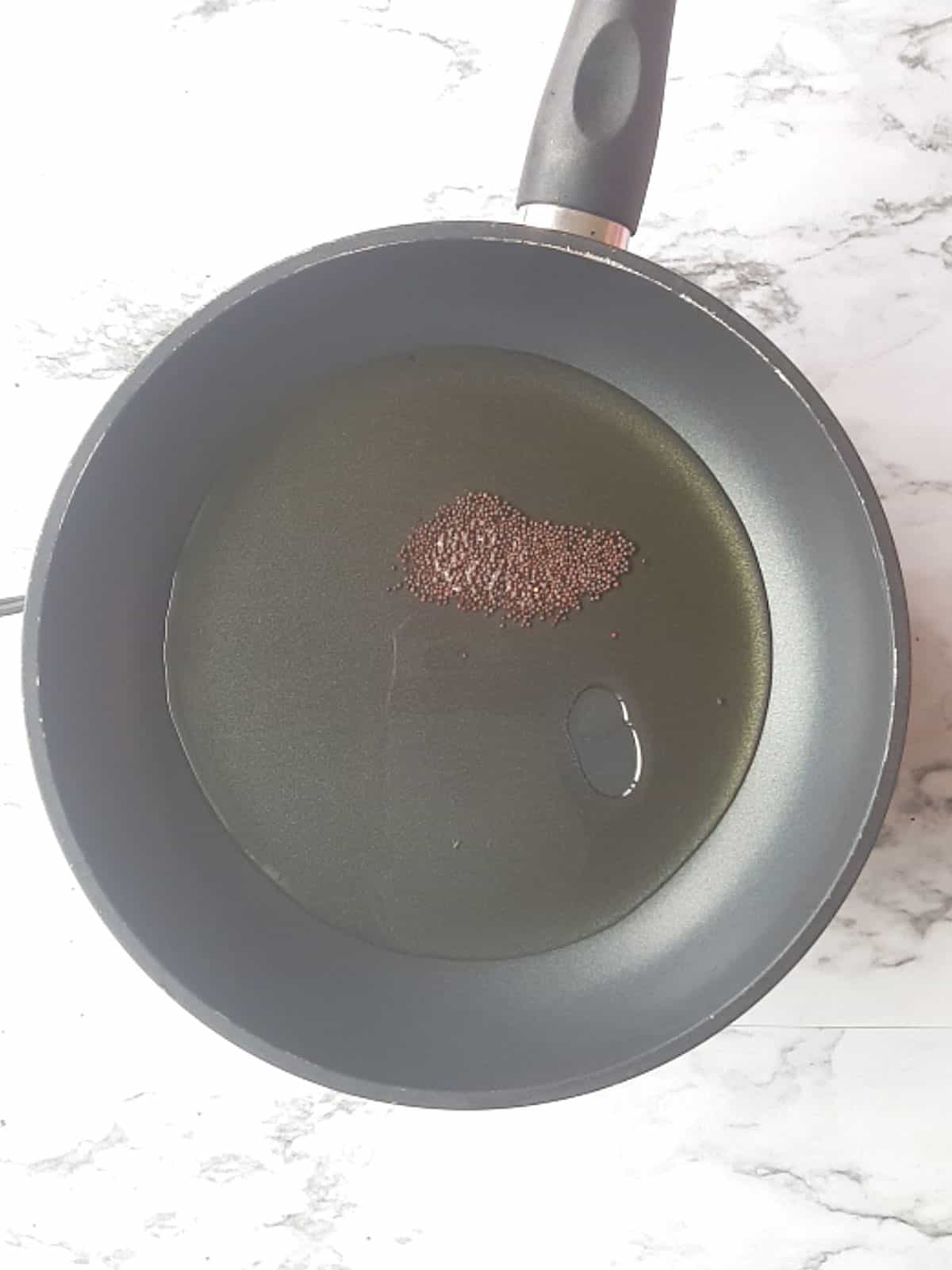 mustard seeds and the oil in the pan for making South indian lemon pickle