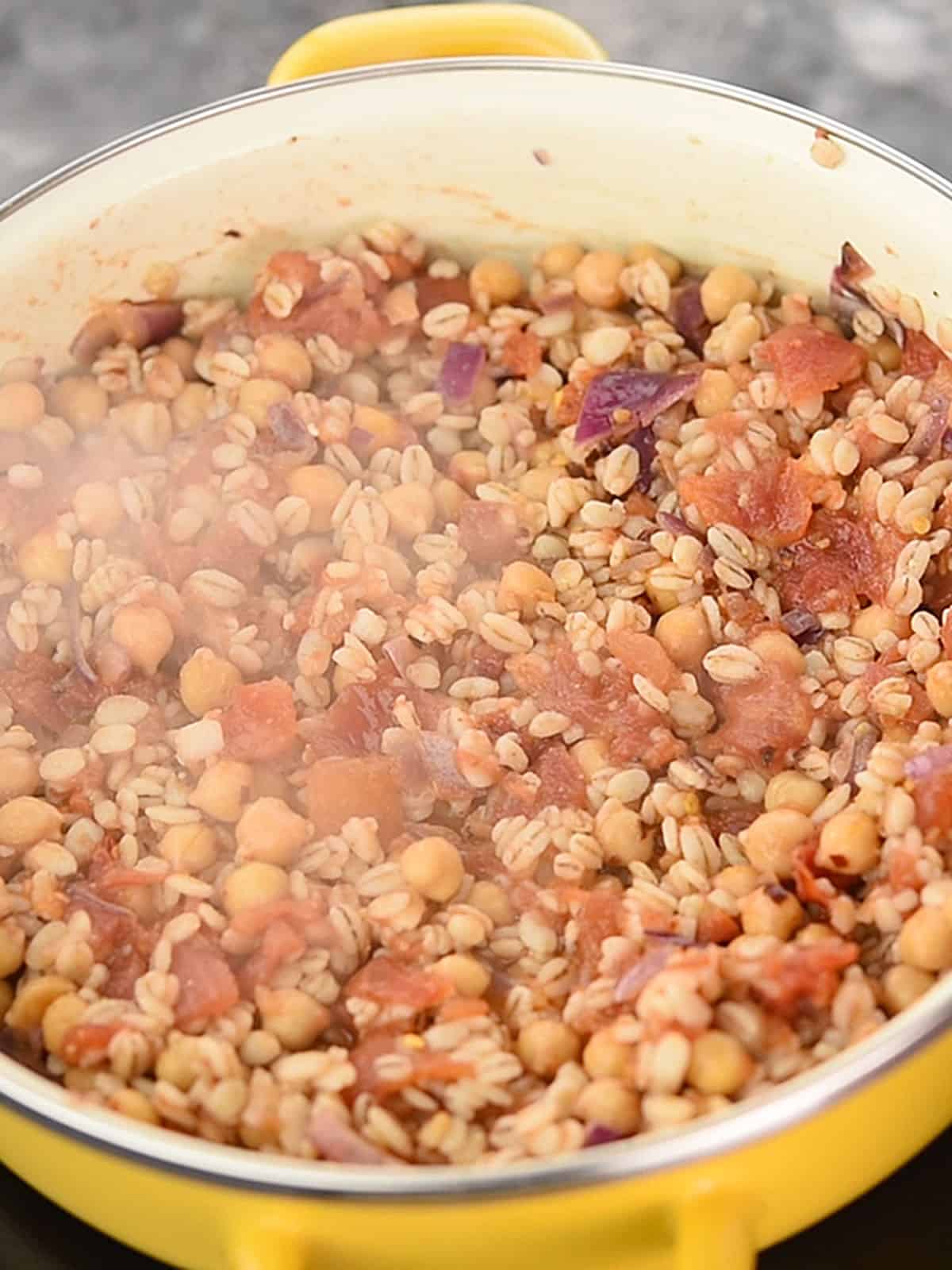 Barley, chickpeas, and diced tomatoes added to the sautéed onions in the pan.