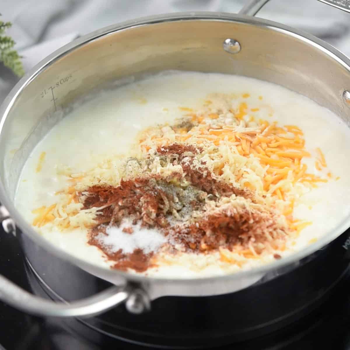 Mixing shredded cheese and spices into a creamy sauce.