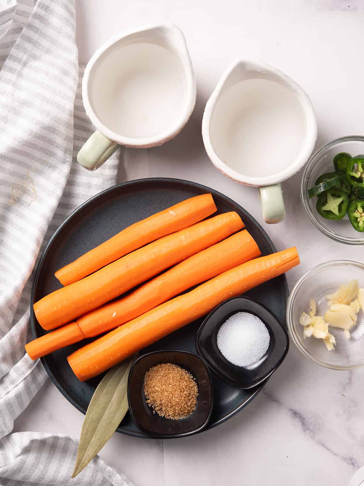 Fresh carrots, jalapeños, garlic cloves, vinegar, and spices laid out on a wooden cutting board for the spicy pickled carrots recipe.