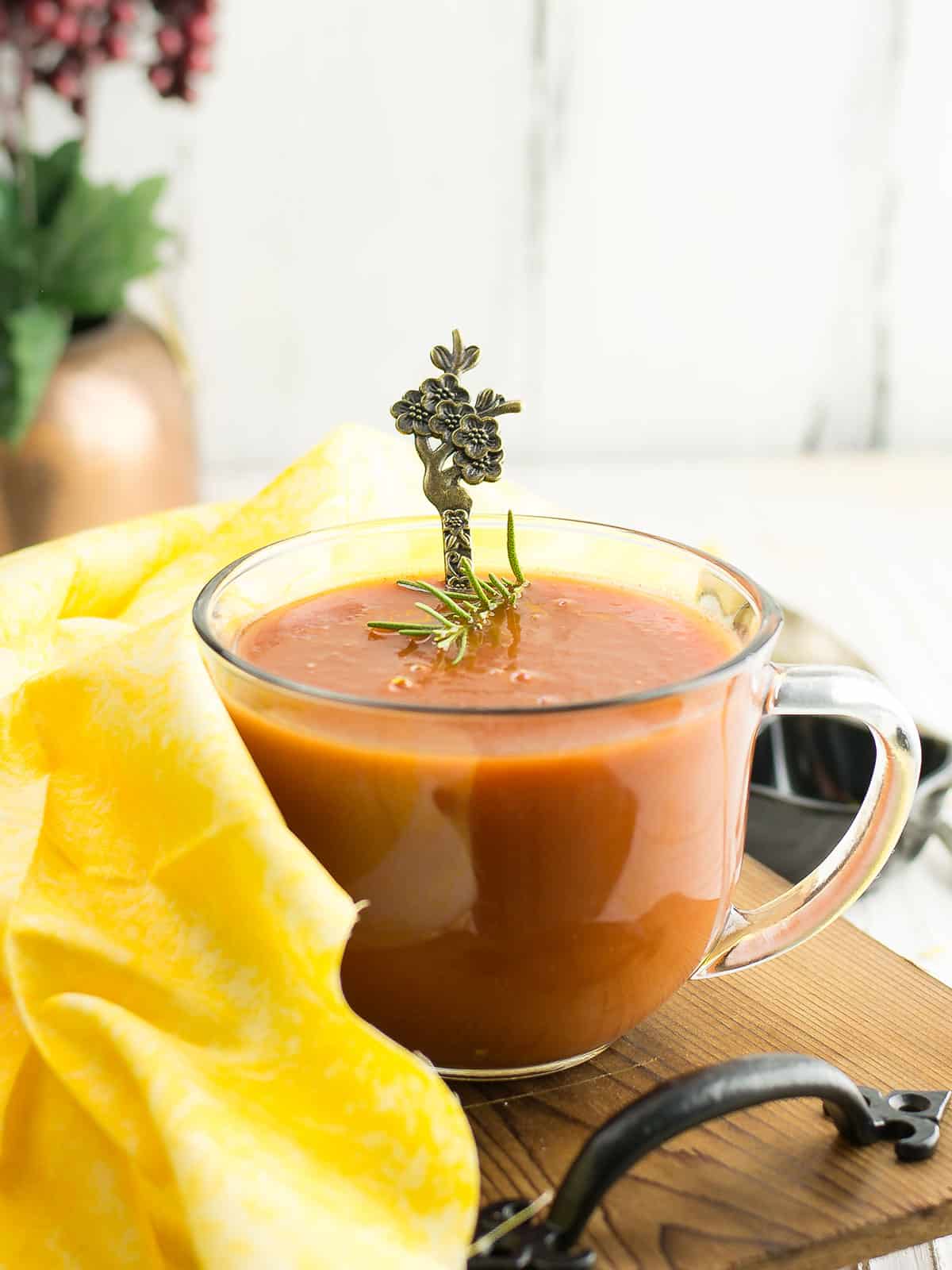 A close-up of the vibrant tomato soup from tomato paste served in a white bowl with a spoon beside it.