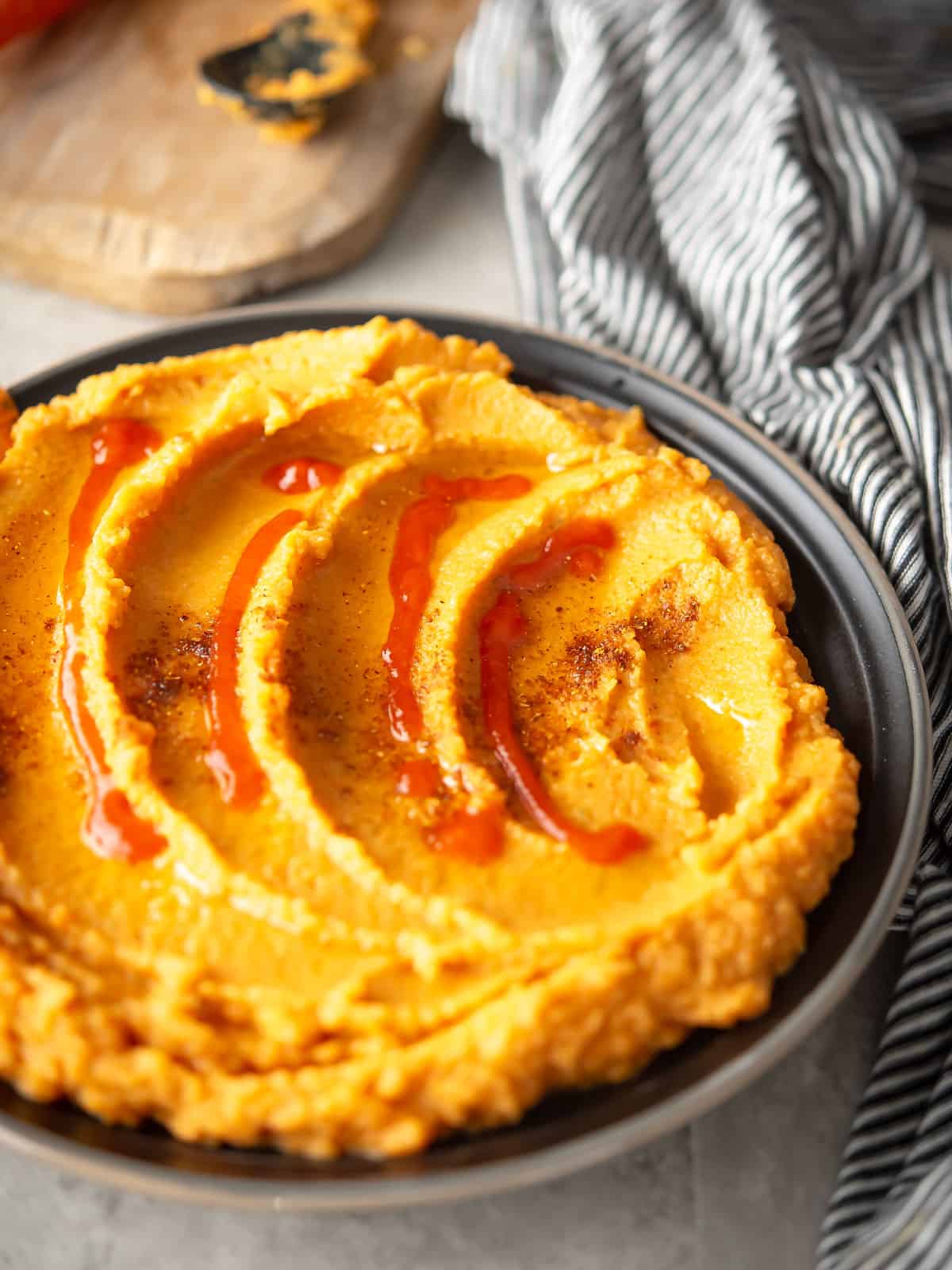 Delicious carrot Sriracha hummus served in a bowl with a drizzle of olive oil.
