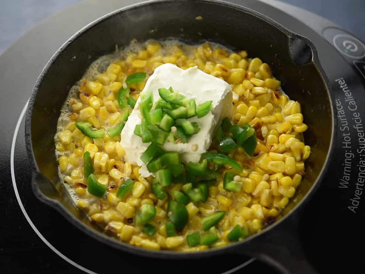 Stirring creamy mixture in a pan to create a silky texture with cream cheese and jalapeno slices