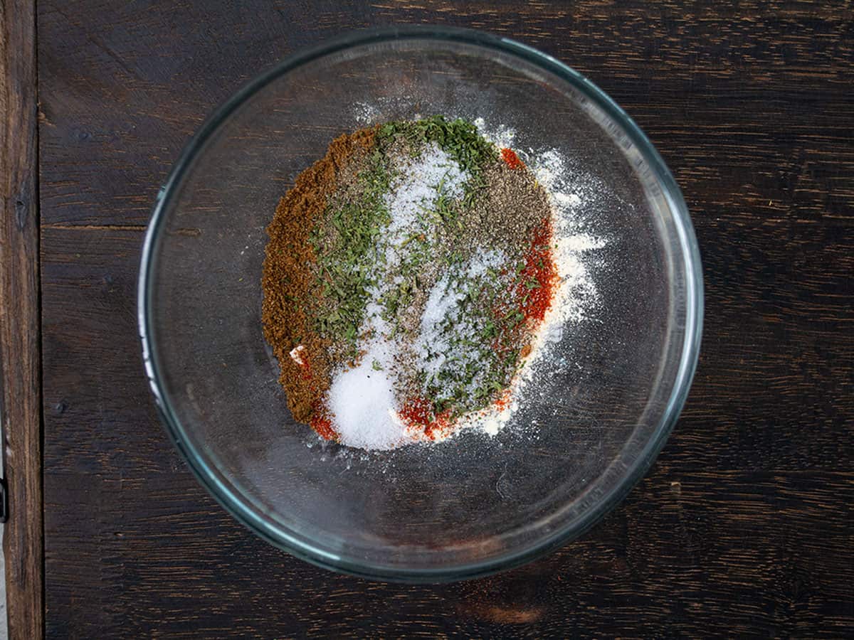 Adding cayenne pepper, cumin, and other ingredients to the bowl for seasoning.