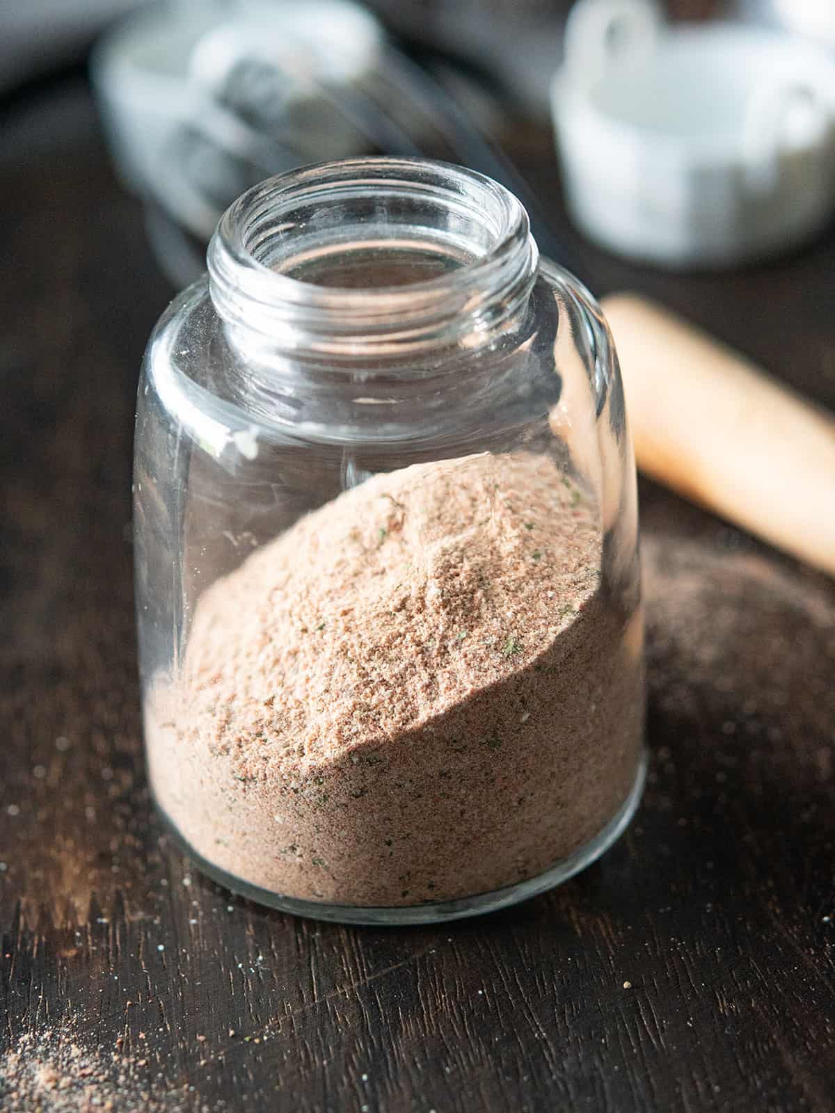 Cuban seasoning mix ingredients in a clear glass jar on a kitchen counter