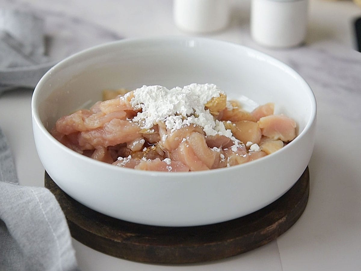 Chicken marinating in a bowl with soy sauce, rice wine vinegar, and cornstarch.