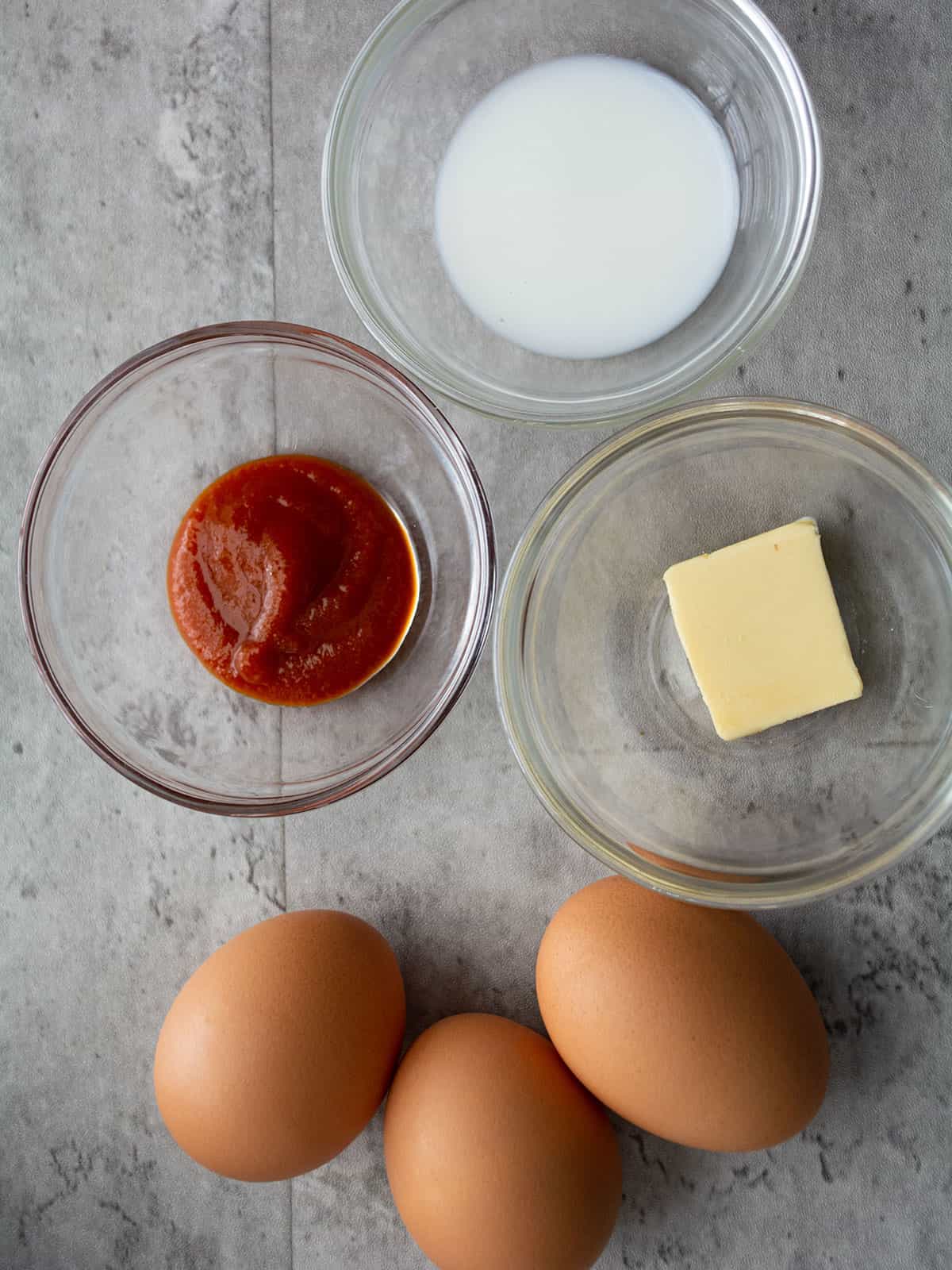 Ingredients for Sriracha scrambled eggs: eggs, milk, Sriracha sauce, and butter.
