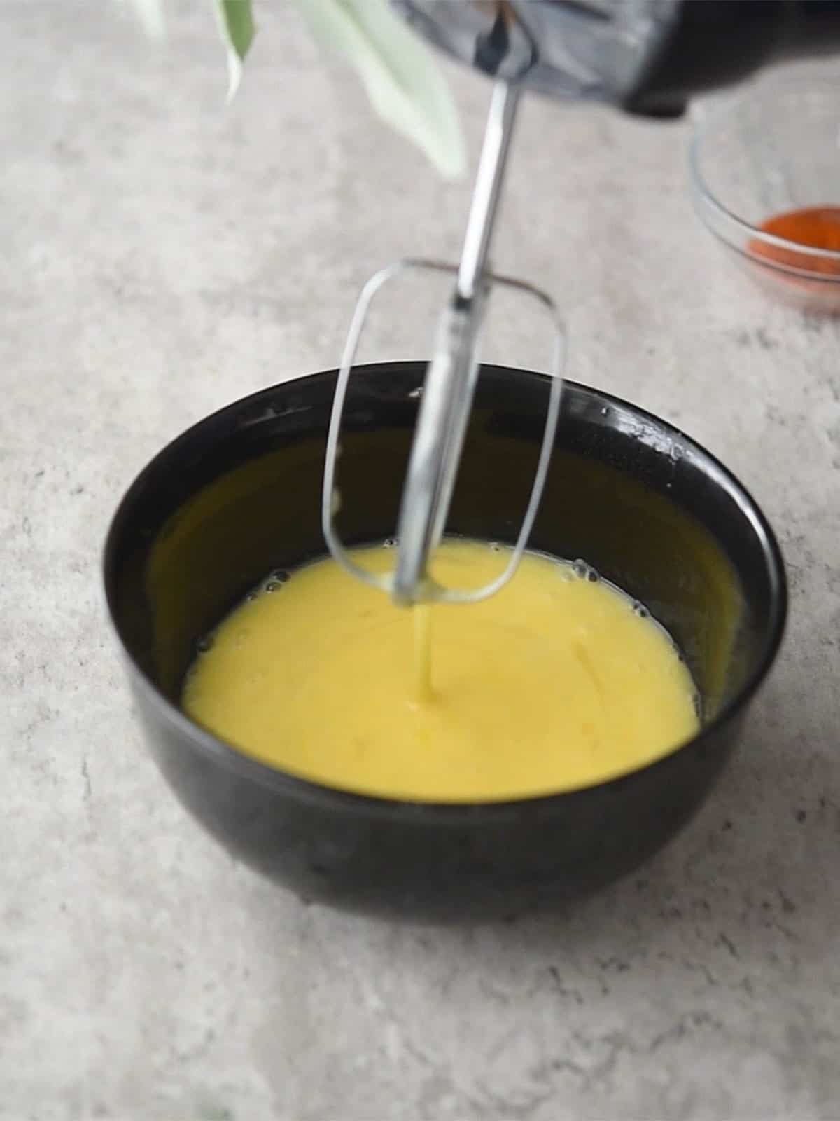 Mixing eggs, milk, and Sriracha sauce in a bowl.