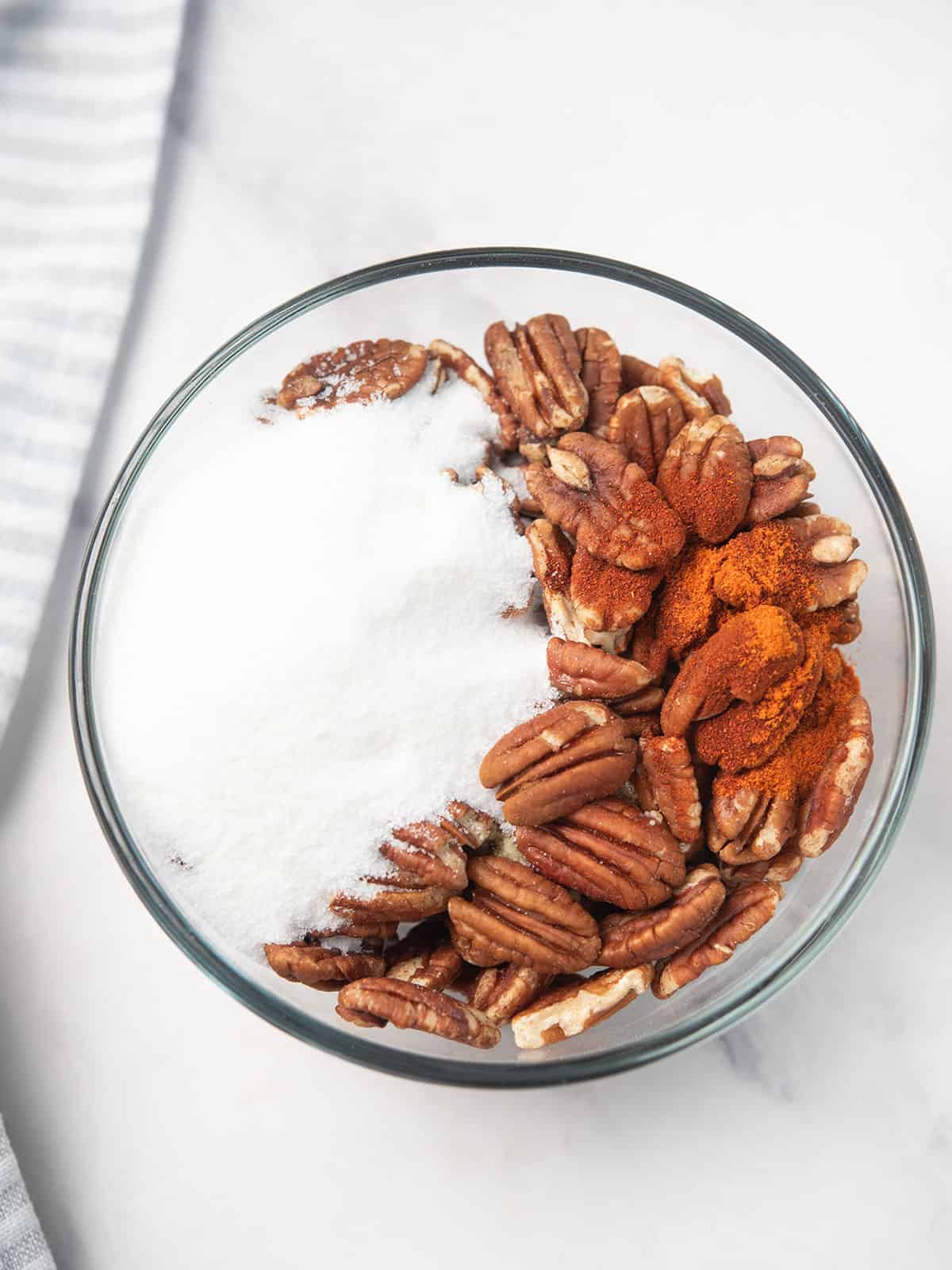 adding sugar to the pecans in a bowl, ready for baking.