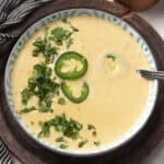 A bowl of smooth jalapeño soup with a spoon and the cilantro