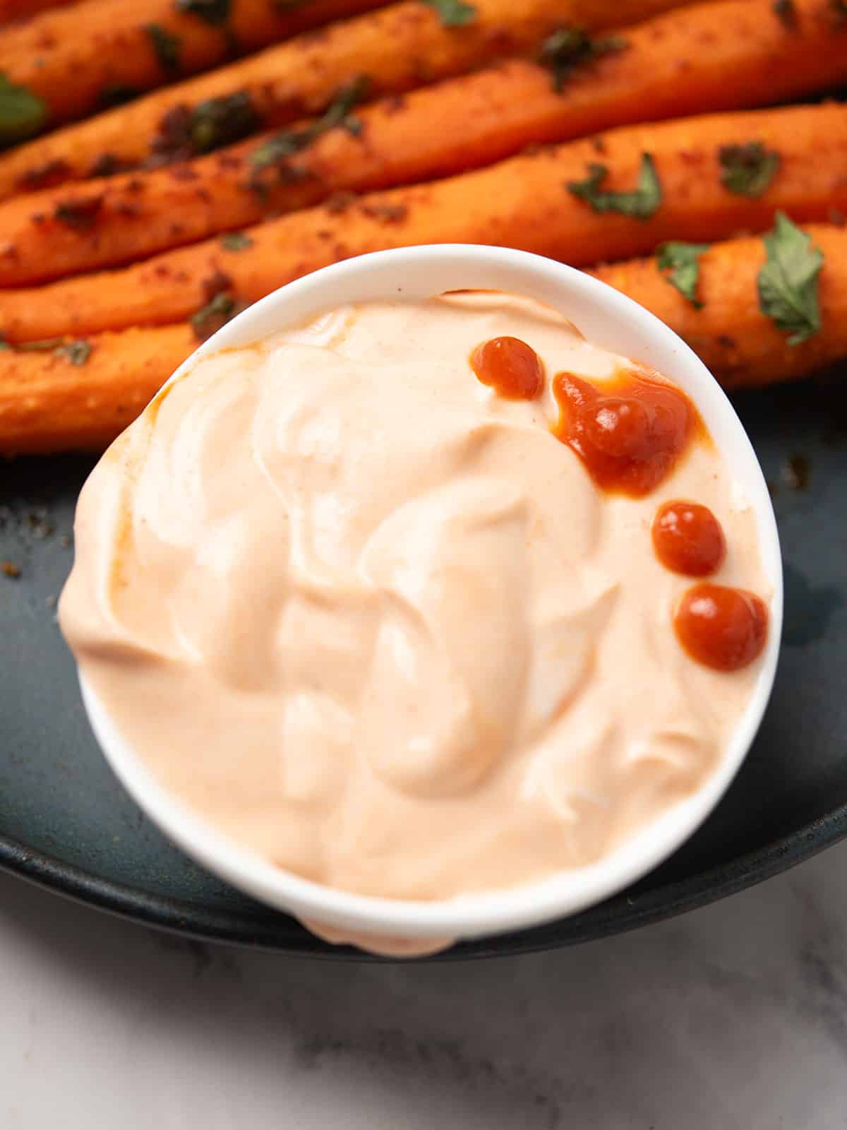 Creamy Greek yogurt Sriracha sauce in a bowl with a drizzle.