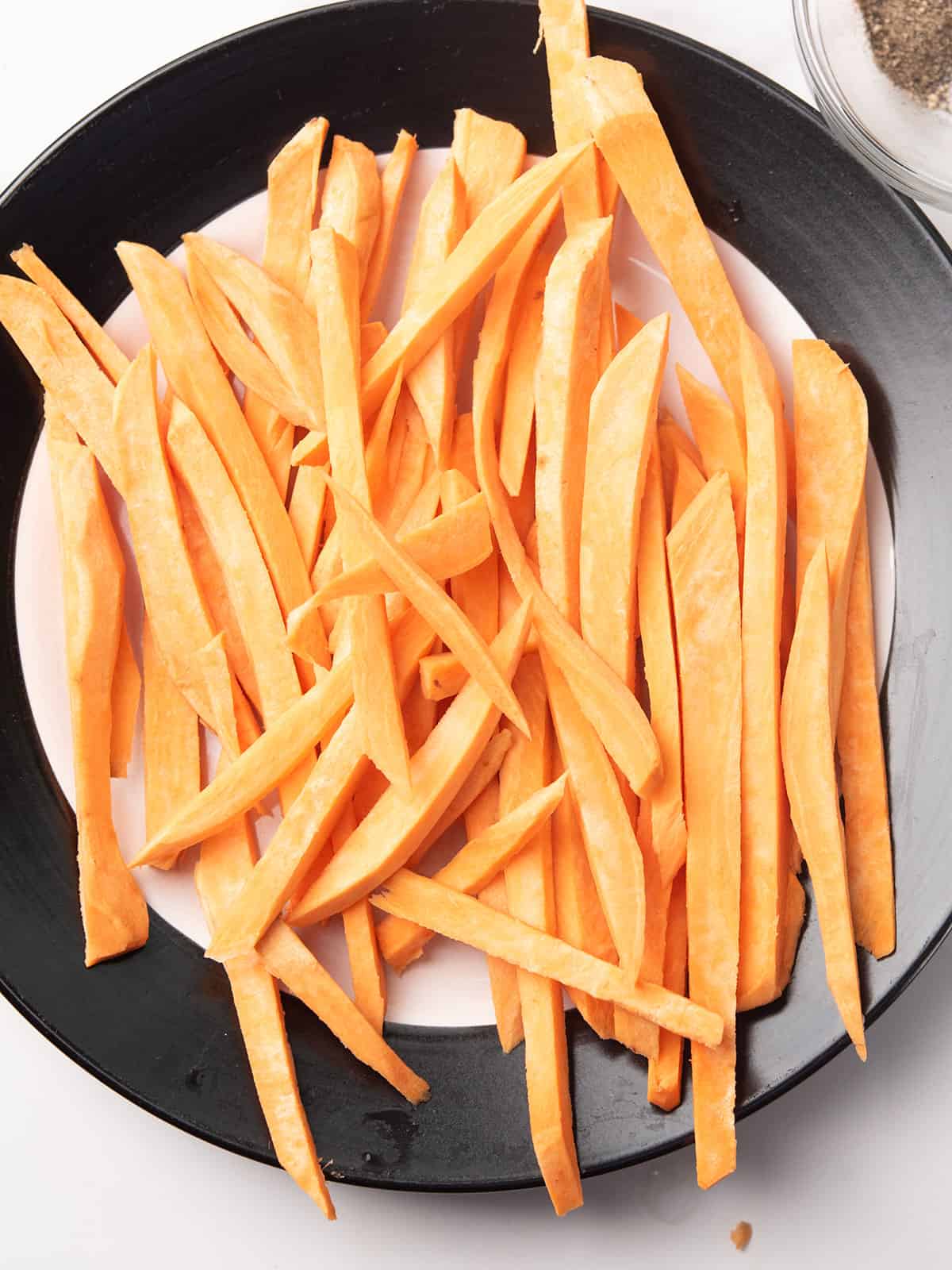 Sweet potatoes being sliced into uniform fries on a cutting board.