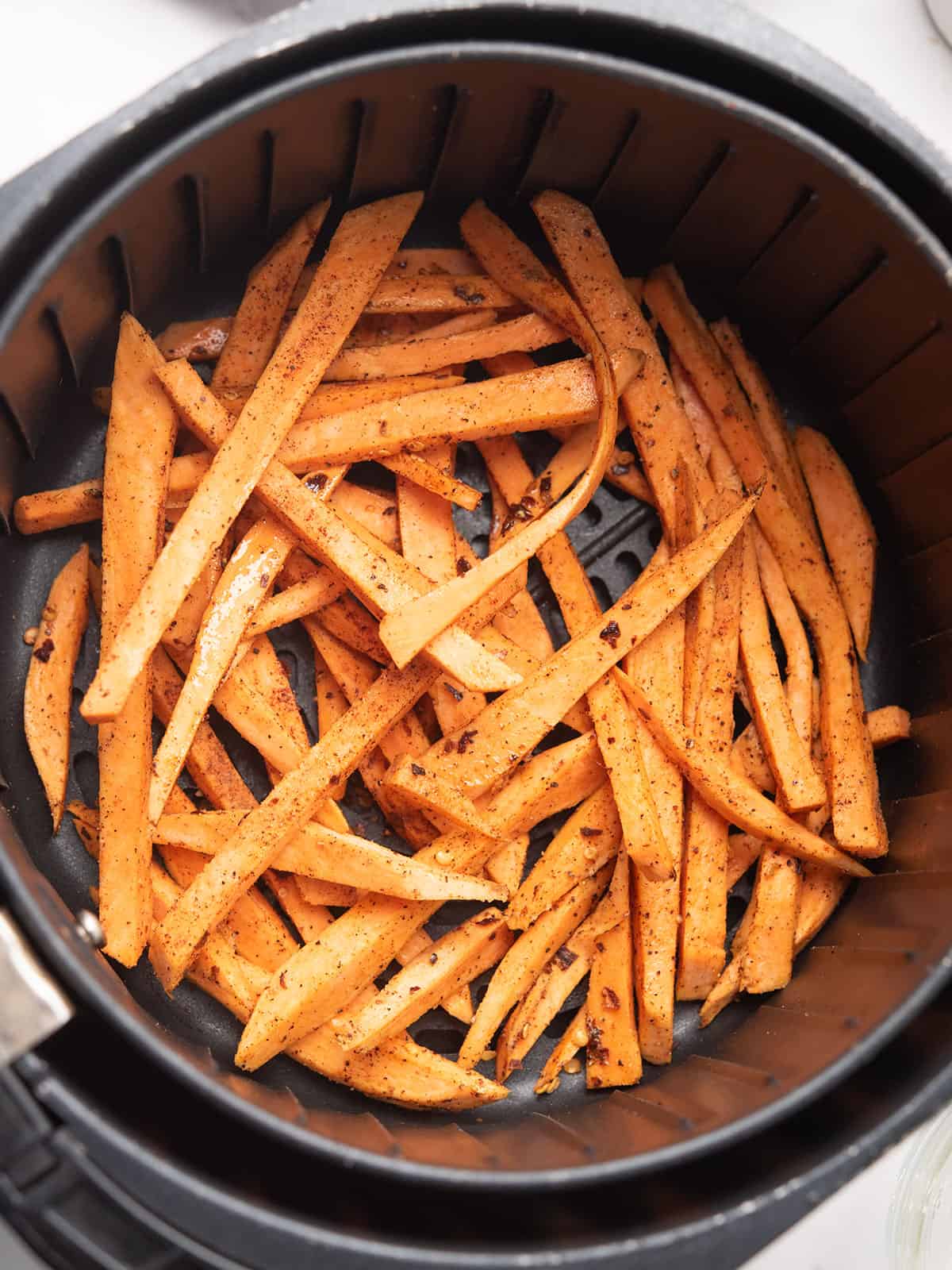 Seasoned sweet potato fries arranged in a air fryer.