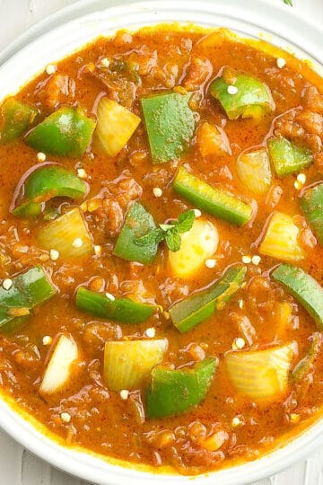Bell pepper curry is made with onions, tomatoes served in a white bowl.