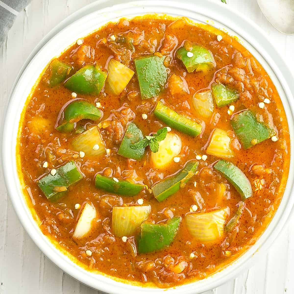 Bell pepper curry is made with onions, tomatoes served in a white bowl.