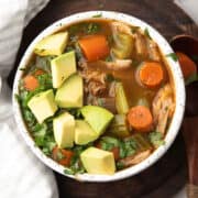 cilantro chicken soup served in a white bowl garnished with avocado and fresh cilantro