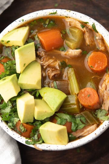 cilantro chicken soup served in a white bowl garnished with avocado and fresh cilantro