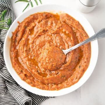 Roasted veggie sauce with tomato and garlic in a white bowl with a spoon.
