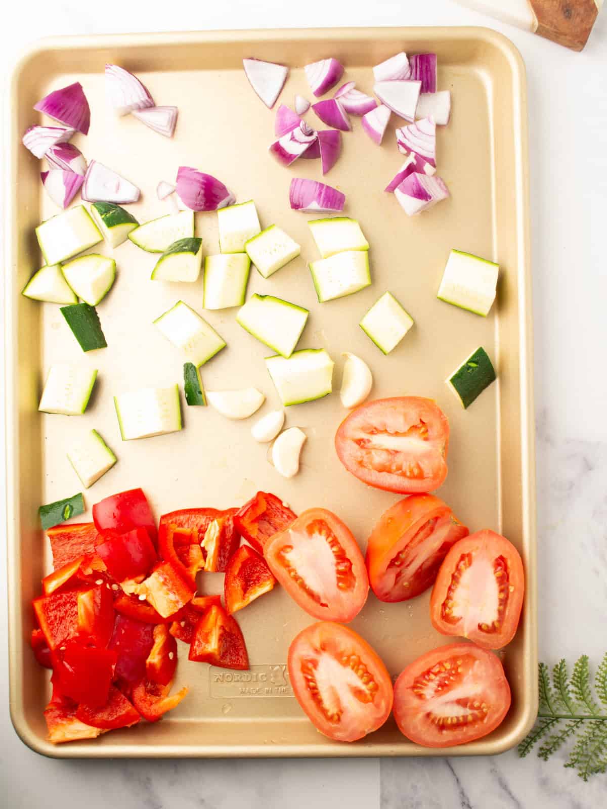 Chopped vegetables seasoned with olive oil and spices on a baking sheet.