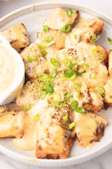 Crispy air-fried Bang Bang Salmon Bites drizzled with a creamy, spicy sauce, garnished with green onions and sesame seeds