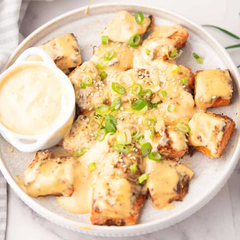 Crispy air-fried Bang Bang Salmon Bites drizzled with a creamy, spicy sauce, garnished with green onions and sesame seeds