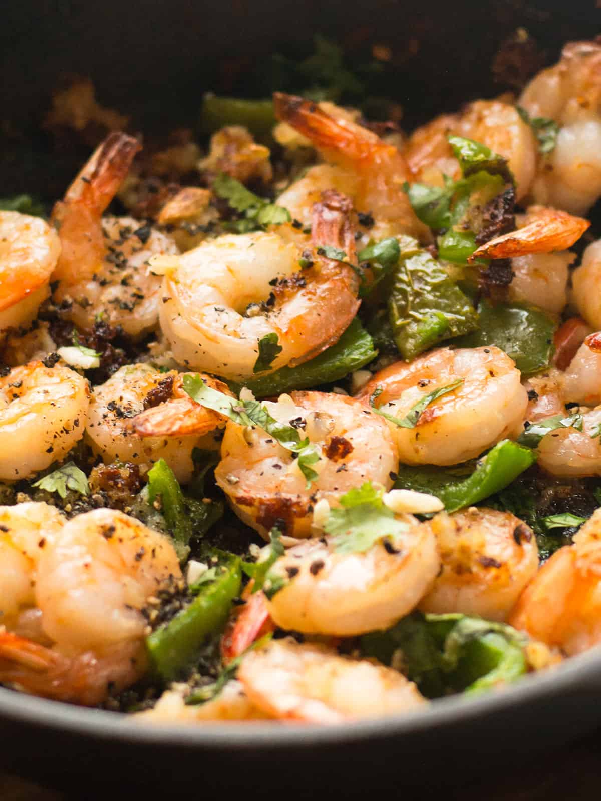 A close view of juicy garlic pepper shrimp in the skillet garnished with ground black pepper.