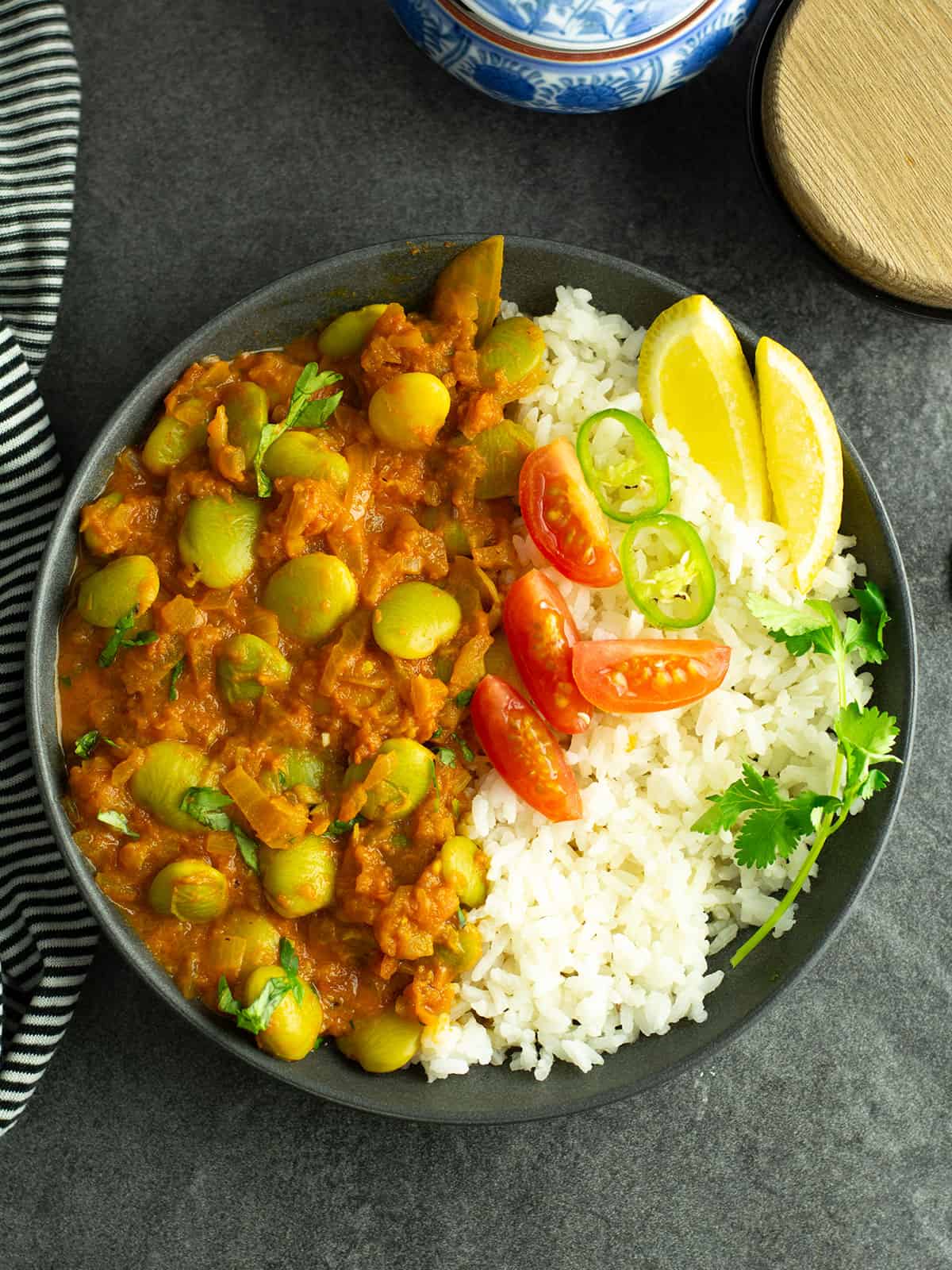lima bean curry served in a place with rice and garnished with lemon wedges and cilantro