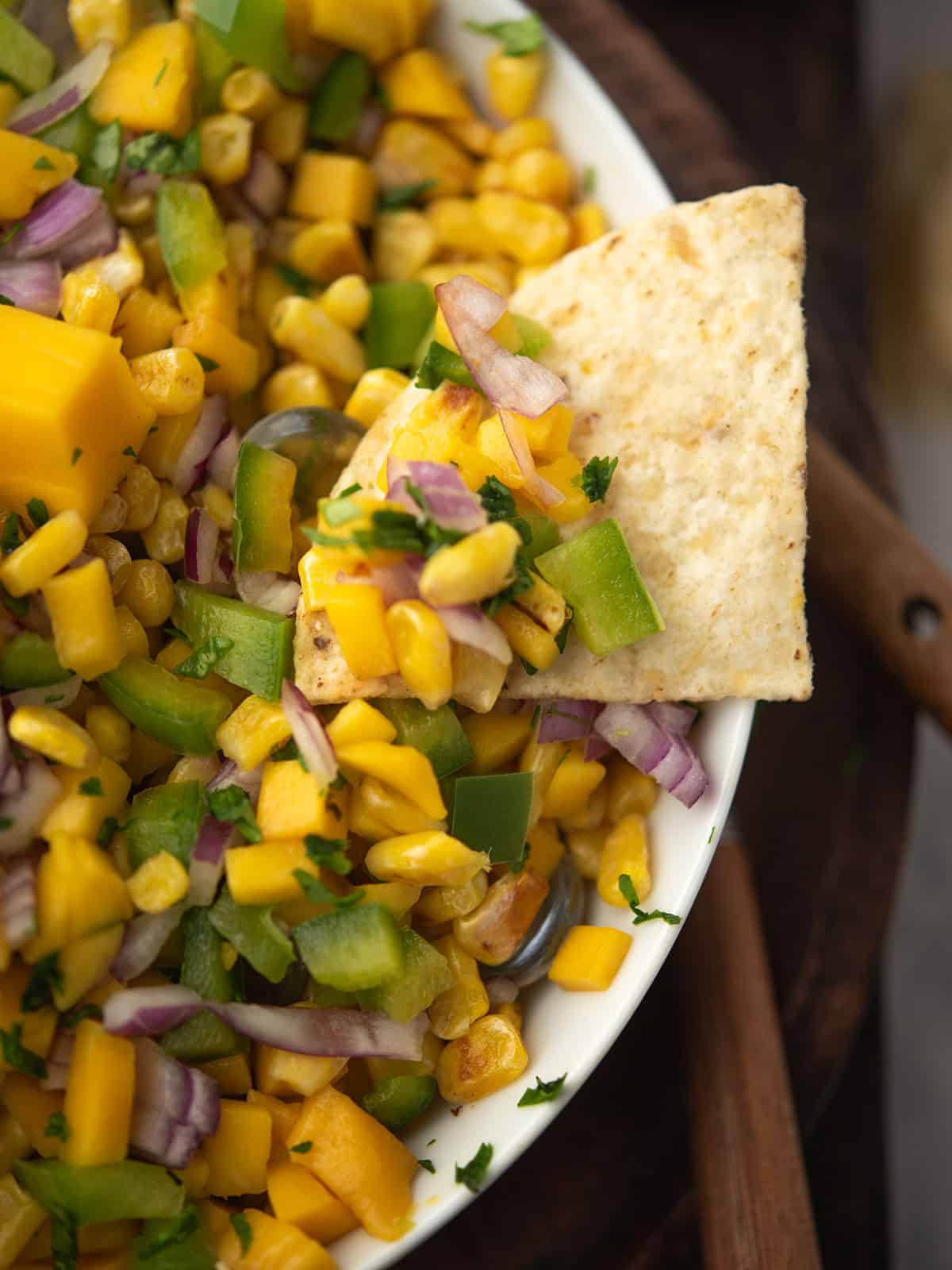 Delicious mango corn salsa served with tortilla chips on a wooden table.