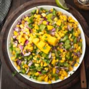 mango corn salsa garnished with cilantro served in a bowl lime wedges.