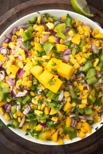 mango corn salsa garnished with cilantro served in a bowl lime wedges.