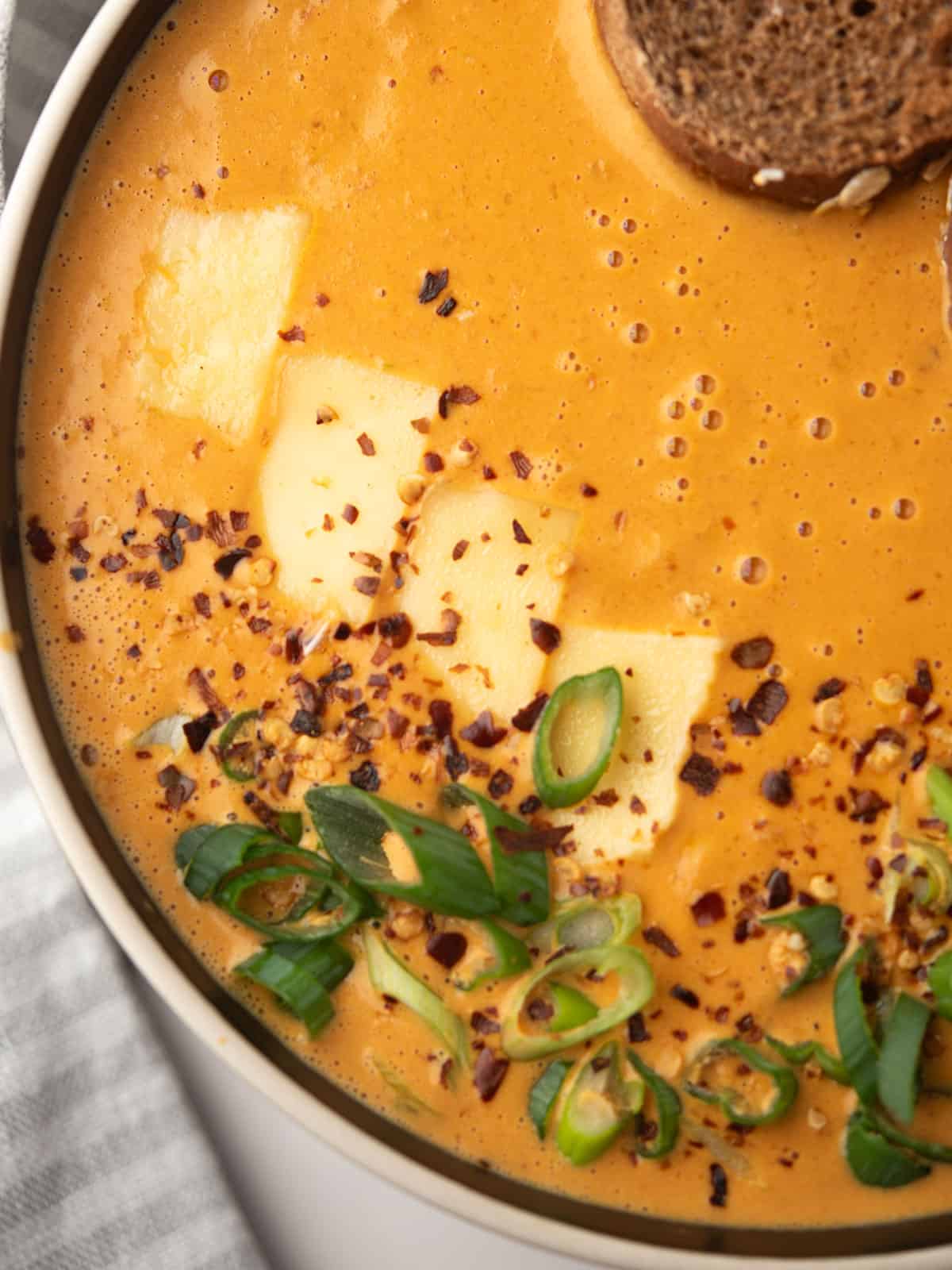 Close-up of the rich, orange soup with melted cheese on top.
