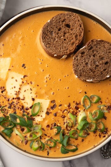 This Red Pepper Gouda Soup served in a bowl, garnished with chopped green onion, and crusty bread for dipping.