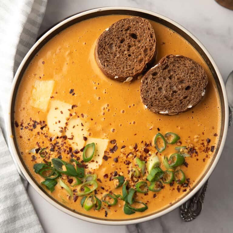 This Red Pepper Gouda Soup served in a bowl, garnished with chopped green onion, and crusty bread for dipping.