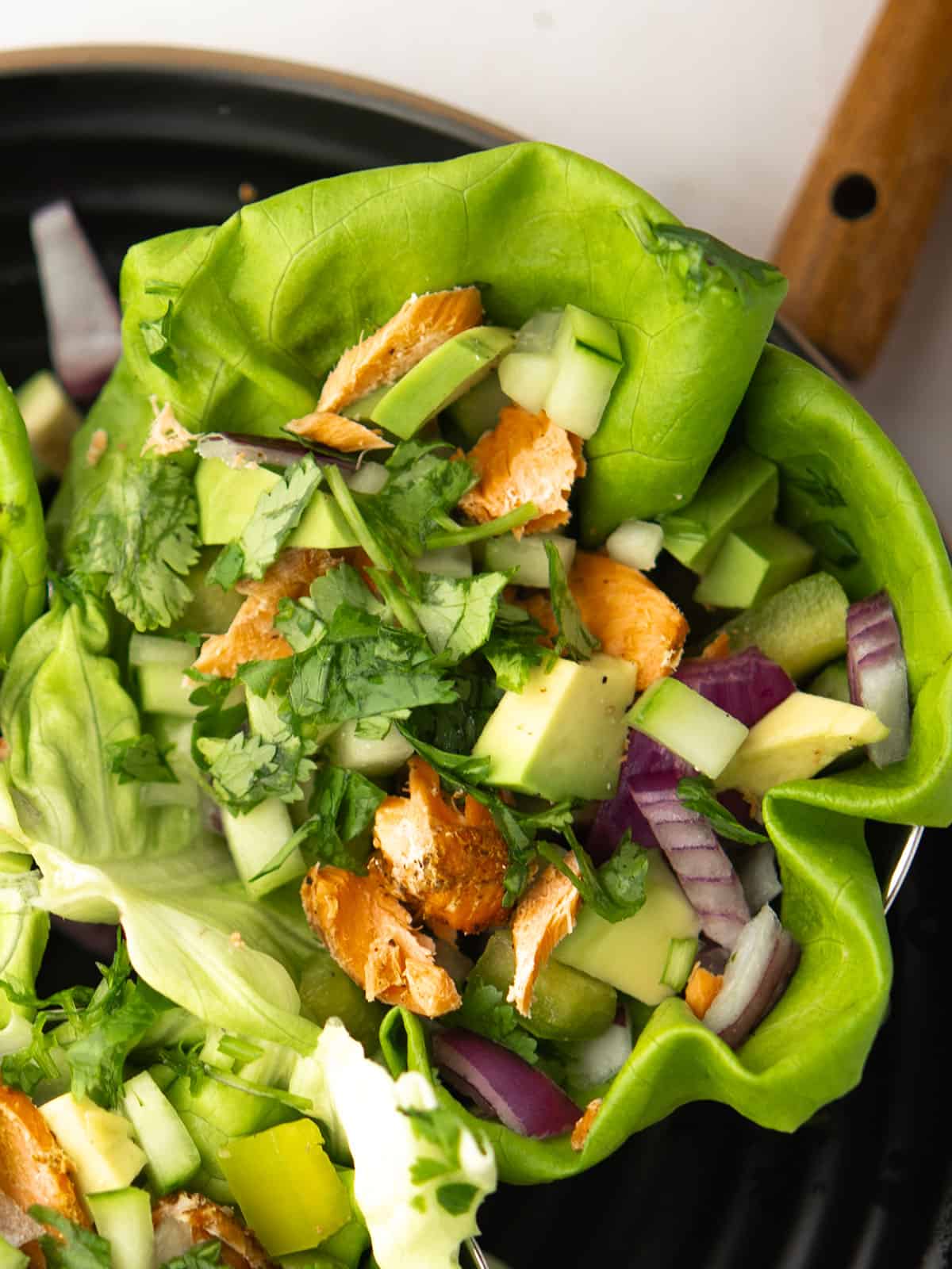 Assembling salmon lettuce wraps with fresh toppings on lettuce leaves.
